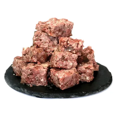 Ułożone w stos kostki mięsa na czarnym talerzu, surowe i soczyste, odpowiednie do karmy dla zwierząt.