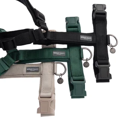 Nomad Tales dog harnesses in black, green and beige with metal rings and brand tags.