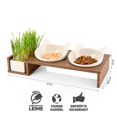 Comedouro elevado em madeira com duas taças de cerâmica em forma de orelhas de gato, recipiente para erva, dimensões 41×19,5×11 cm. Texto visível: 100% UNBEDENKLICHE LEIME, FAIRER HANDEL, GEPRÜFTE SICHERHEIT.