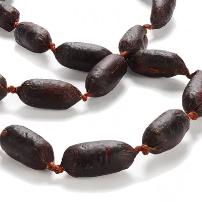 Chapelet de petites saucisses sèches brunes, attachées par des liens à chaque extrémité, présentées sur fond blanc. Aucun emballage ou marque visible.