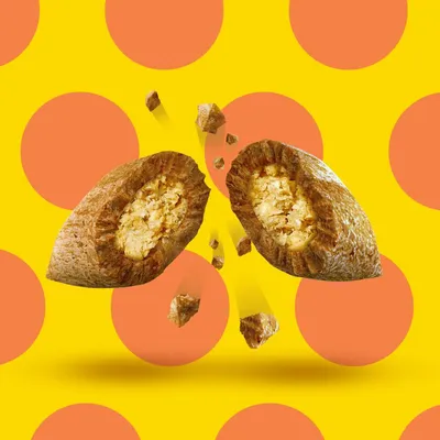 Croqueta de pienso partida por la mitad, mostrando relleno interior y trozos pequeños alrededor. Fondo amarillo con círculos naranjas.