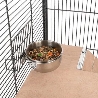 Gamelle en acier inoxydable avec graines et légumes, fixée à une cage métallique au-dessus d'une plateforme en bois.