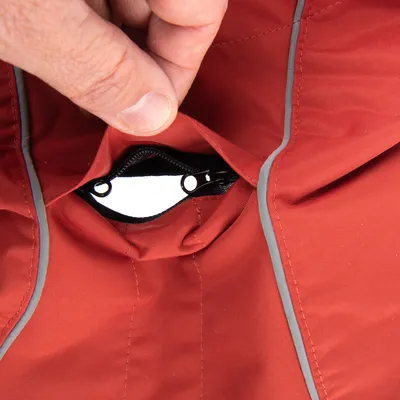 Close-up van een rode jas met reflecterende strepen en een klein ritsvakje dat door een hand wordt geopend.