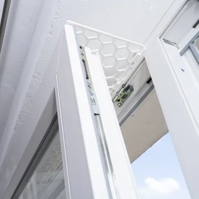 Okenní ochranná mřížka s voštinovou strukturou, namontovaná na otevřeném okně. Ochrana proti vypadnutí nebo útěku domácích mazlíčků.