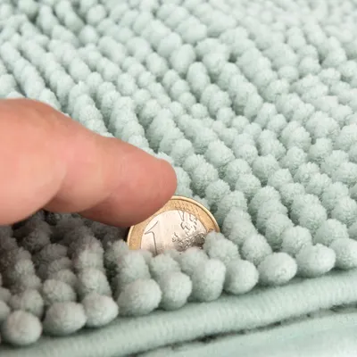 Zbliżenie na jasnozieloną, teksturowaną matę z palcem i monetą 1 euro pokazującą grubość materiału.