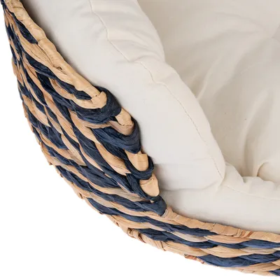 Detailaufnahme eines geflochtenen Korbs in Blau und Naturtönen mit beigem Stoffkissen.