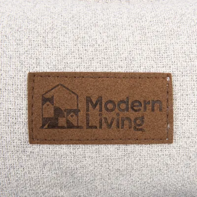 Modern Living. Logotyp på brun tygetikett, fäst på ljusgrått textilmaterial.