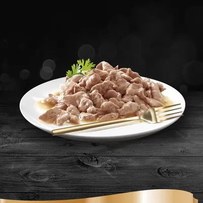 Nahaufnahme eines Tellers mit saftigen Fleischstücken in Sauce, dekoriert mit Petersilie und einer goldenen Gabel. Dunkler Hintergrund.