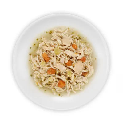 Primo piano di carne di pollo tritata con carote, patate ed erbe in brodo su un piatto bianco.