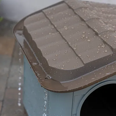 Nahaufnahme eines braunen, wasserabweisenden Dachs mit ablaufendem Regenwasser auf einer Hundehütte.