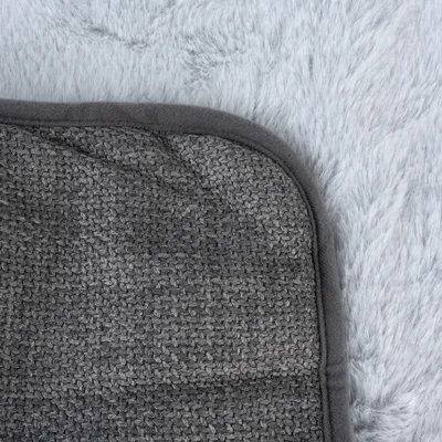 Nahaufnahme einer grauen, strukturierten Matte mit abgerundeten Kanten auf einem flauschigen, weissen Hintergrund.