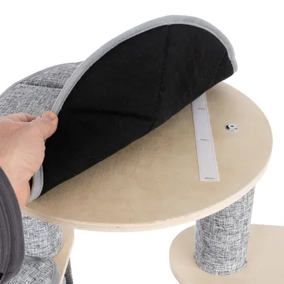 Plateforme en bois clair avec coussin amovible maintenu par une bande auto-agrippante, main soulevant le coussin. Revêtement tissu gris visible sur les poteaux.