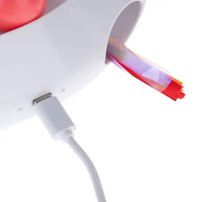 Weisses Gerät mit USB-Anschluss und bunten Stoffstreifen, die aus einer Öffnung herausragen.