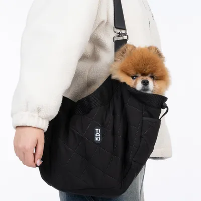 Tiaki black carrier bag with quilted design, dog sitting inside. Adjustable shoulder strap and mesh details visible.