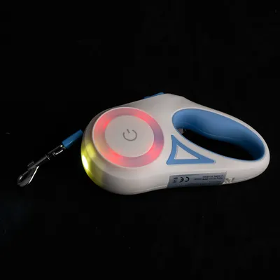 Laisse rétractable blanche et bleue avec poignée, bouton d’alimentation visible, lumières LED rouges et jaunes allumées, mousqueton métallique à l’extrémité du cordon.