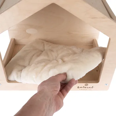 Egy kéz egy puha, krémszínű párnát helyez el egy 'natural paradise' feliratú faházba.