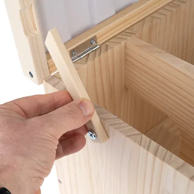 Holzkonstruktion mit Scharnieren. Hand zeigt, wie ein Holzteil eingesetzt wird, um die Box zu stabilisieren oder zu verschliessen.