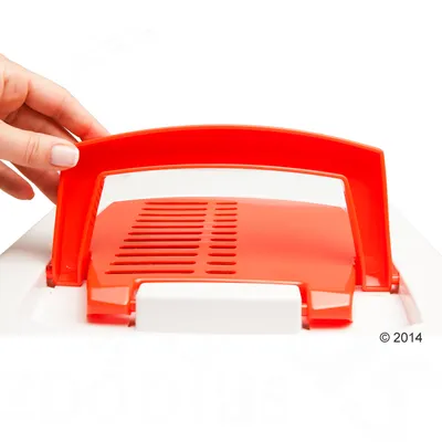 Manico rosso in plastica su trasportino bianco con griglia di aerazione, una mano solleva il manico.