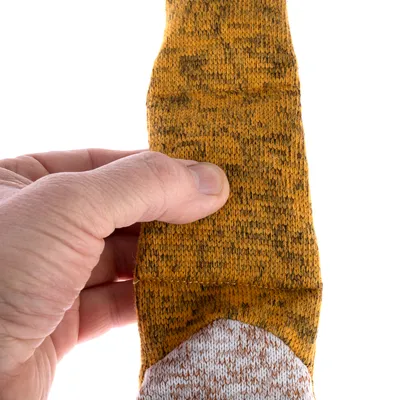 Bližnji posnetek roke, ki drži rumeno-rjavo vzorčen tekstilni trak. Prikaz strukture materiala.