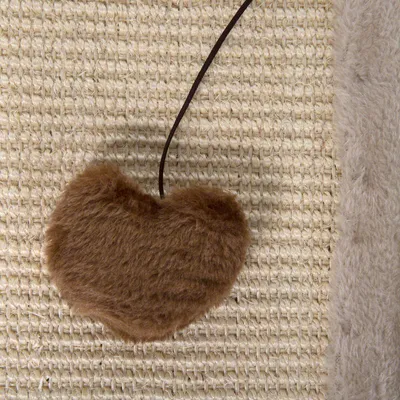 Braunes, herzförmiges Spielzeug aus Plüsch mit Schnur auf einer Sisal-Oberfläche.