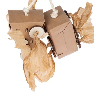Jouet suspendu en carton, bois et papier froissé, composé de deux blocs reliés par une corde épaisse, avec disques en bois et franges en papier visibles.