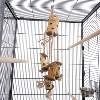 Подвесная игрушка из дерева и веревки с несколькими трубками и платформами, подходит для птичьих клеток. Видна в металлической клетке с жердочками и кормушкой.