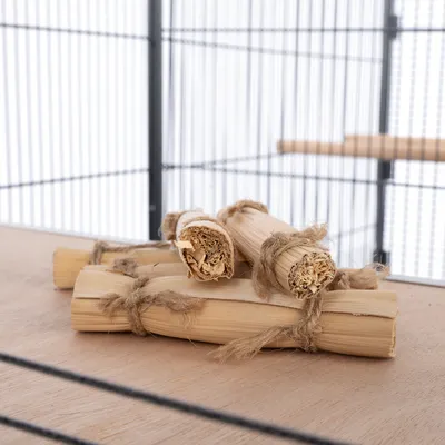 Bâtonnets de bois naturel attachés avec de la ficelle, posés sur le sol d'une cage à barreaux métalliques.
