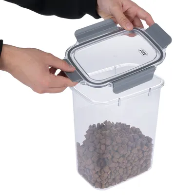 Transparente voercontainer met grijze deksel, geopend. Handen tonen het eenvoudige gebruik van de sluiting. Container gevuld met droogvoer.