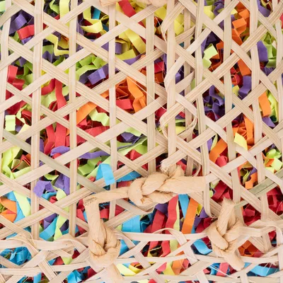 Gros plan sur un panier en osier tressé rempli de bandes de papier colorées. Matériaux visibles : osier, papier multicolore.