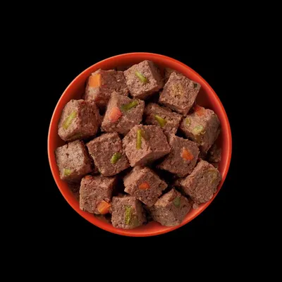 Rote Schale mit fleischbasierten Würfeln, die grüne und orange Gemüsestücke enthalten.