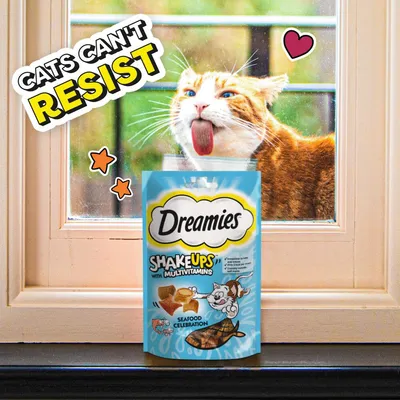 Dreamies Shake Ups with Multivitamins Seafood Celebration treats pack in front of a window, text reads 'Cats can't resist', with cartoon stars and heart.