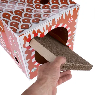 Hand zieht eine Kratzpappe aus einem rot-weiss dekorierten Karton mit Lebkuchenhaus-Motiv.