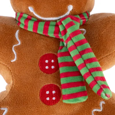 Jouet en peluche en forme de bonhomme pain d’épices, écharpe rayée rouge et verte, deux boutons rouges brodés, tissu doux marron avec détails blancs cousus.