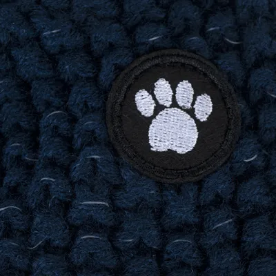 Nahaufnahme eines dunkelblauen Strickmaterials mit einem schwarzen Aufnäher, der eine weisse Pfotenstickerei zeigt.