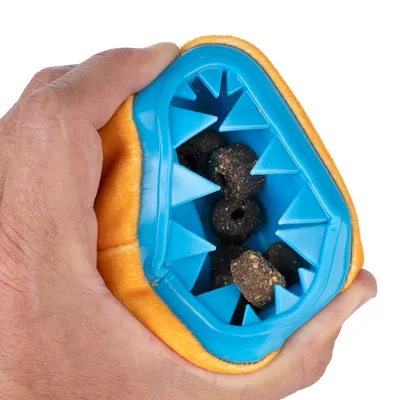 Hand håller en orange-blå leksak med taggar, fylld med mörka godbitar. Visar möjlighet att fylla snacks i interaktiv leksak.