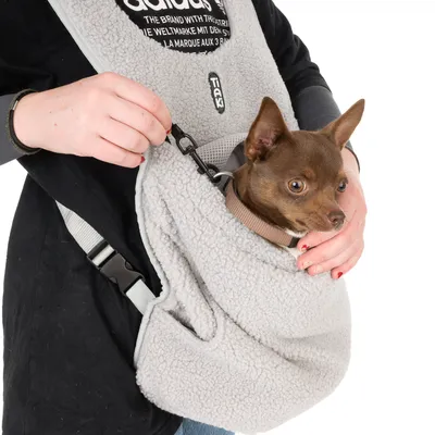 Sac de transport en tissu polaire gris avec sangle, chien marron à l’intérieur, mousqueton de sécurité visible, main tenant le sac. Marque TAK visible sur le sac.