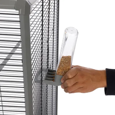 Hand places a transparent feeder with seeds into a holder on a grey cage.