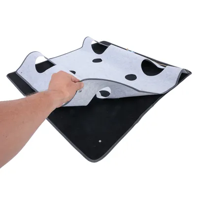 Tapis en feutre gris et noir avec plusieurs trous ronds, une main soulève la partie supérieure pour montrer l’intérieur. Matériau visible : feutre.
