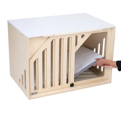 Holz-Hundebox mit weissem Deckel und seitlichen Lüftungsschlitzen. Hand legt ein Kissen in die Box.
