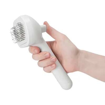Hand holding a white brush with metal bristles, suitable for coat care.