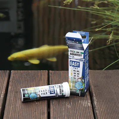 JBL ProAquaTest Easy 7in1 do analizy wody. Testuje NO2, NO3, GH, KH, pH, Cl2 i CO2. Opakowanie i paski testowe na tle stawu.