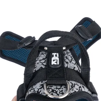 TIKI Hundegeschirr mit reflektierendem Muster, schwarzem Griff und Metallring. Verstellbare Gurte und gepolsterte blaue Innenseite sichtbar.