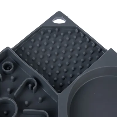 Gros plan sur un plateau compartimenté en plastique gris avec différentes zones texturées à picots et motifs, trou d’accroche visible dans un coin.
