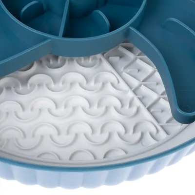 Közelkép egy kerek etetőjátékról kék külső peremmel és fehér, hullám- és nyílmintás, strukturált felülettel.