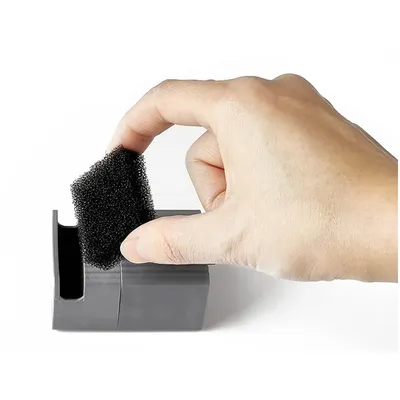 Hand zeigt, wie ein schwarzer Schaumstofffilter aus einem grauen Behälter entnommen wird.