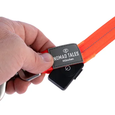 Nomad Tales München Hundeleine in leuchtendem Orange mit reflektierenden Nähten und schwarzem Verschluss, gehalten von einer Hand.