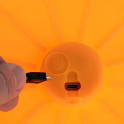 Nærbillede af en orange enhed med USB-C-port og tænd/sluk-knap. Hånd holder et stik til tilslutning.