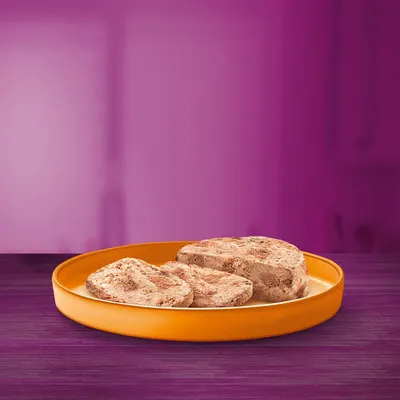 Krupan prikaz tri komada mokre hrane na narančastom tanjuru na ljubičastoj podlozi.