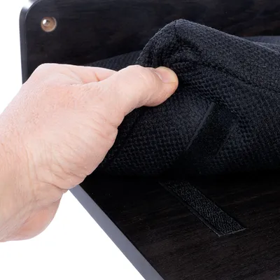 Una mano solleva un tappetino in tessuto nero strutturato con chiusura a strappo da una superficie in legno scuro.