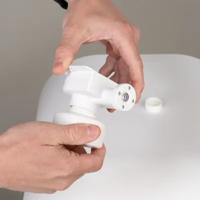 Hands showing the assembly of a white dispenser with screw cap on a container lid.